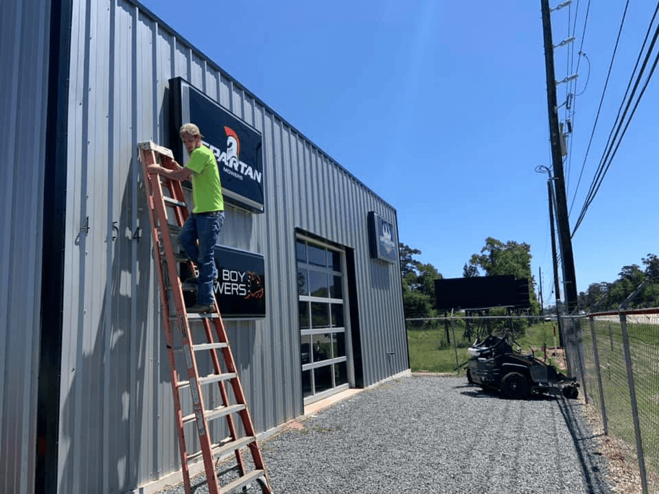 Person standing on a ladder outside a building with signage on a sunny day.