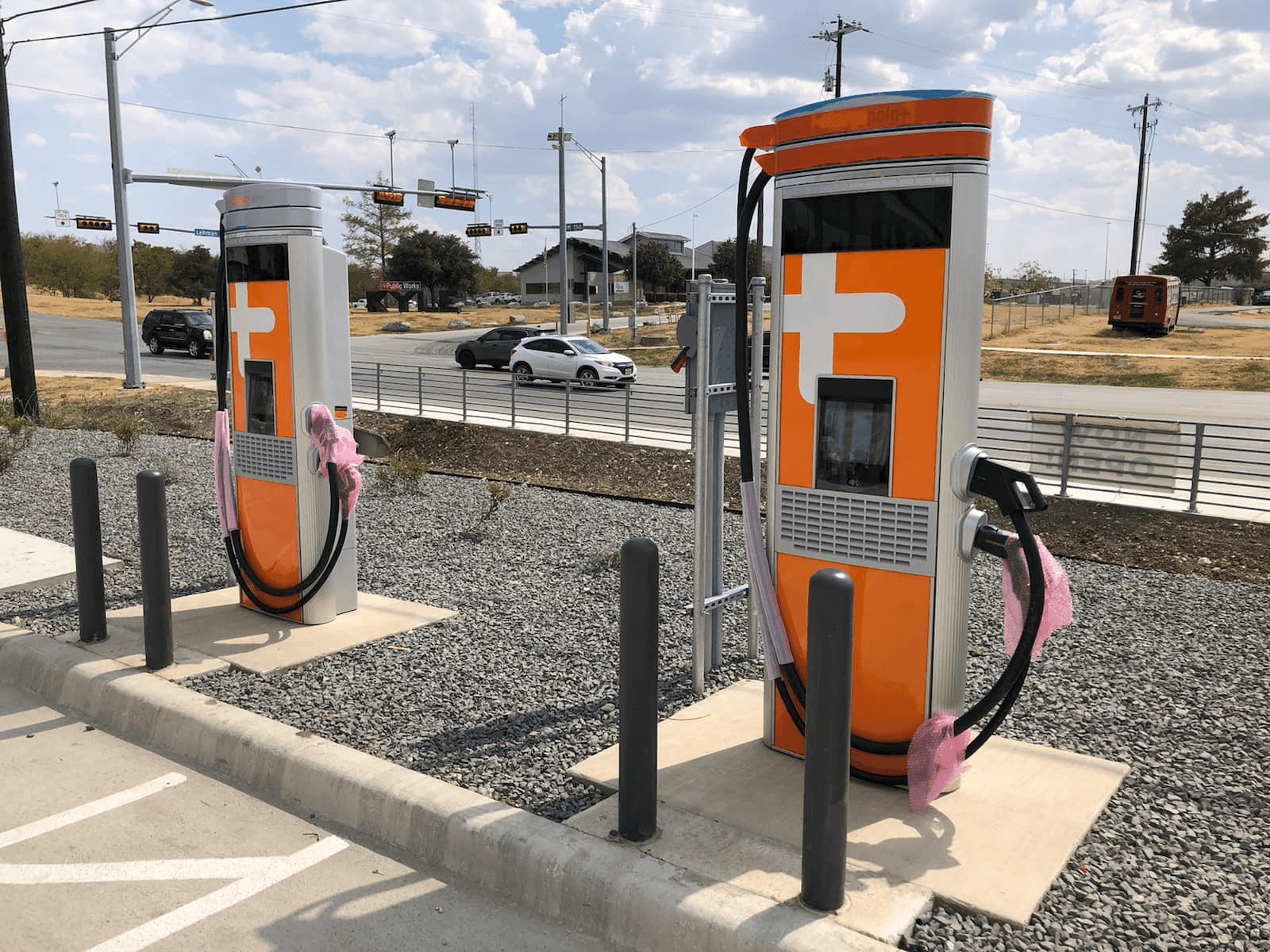 Electric vehicle charging stations by a roadside with cars passing by.