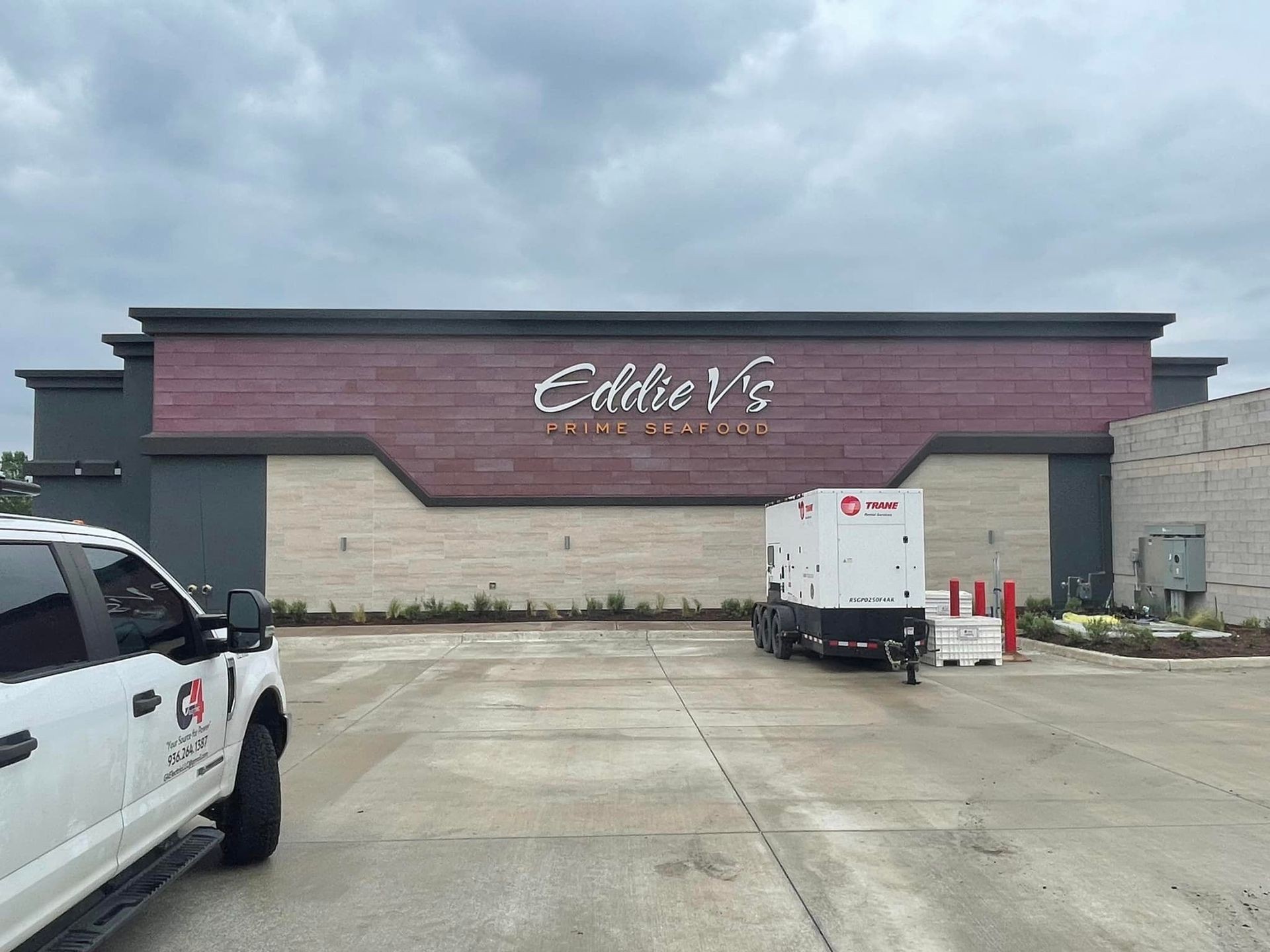 Exterior view of Eddie V's Prime Seafood restaurant with parked truck and equipment trailer in the foreground.