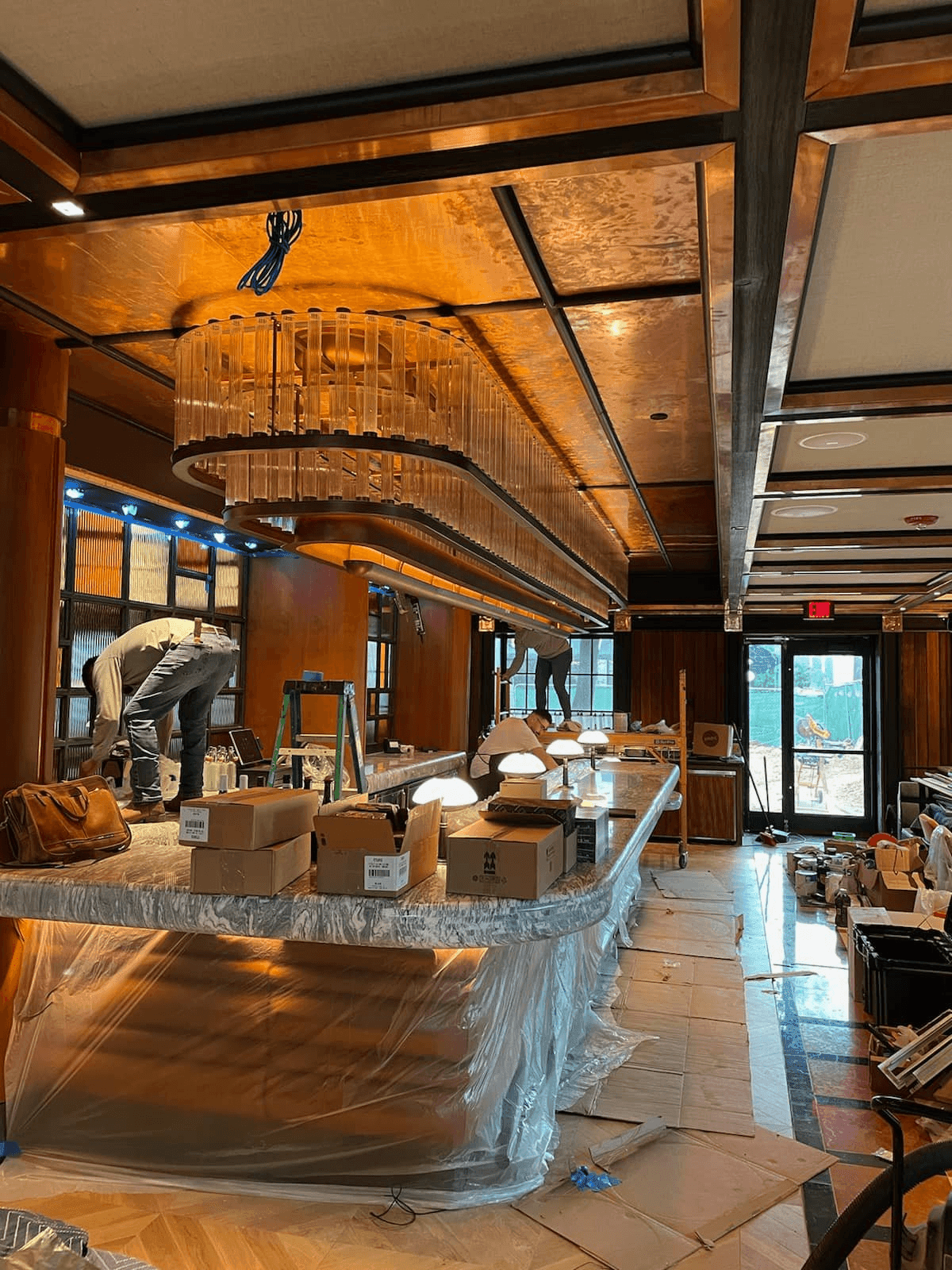 Interior of a bar under construction with workers, cardboard boxes, and covered countertops.